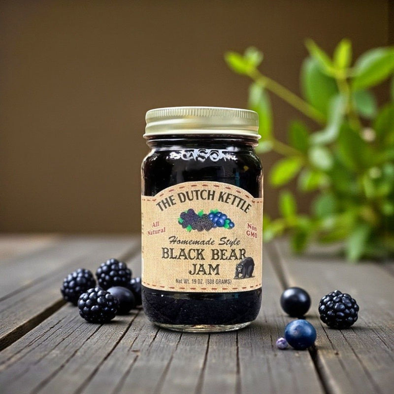 Jar of The Dutch Kettle Black Bear Jam on a wooden surface with blackberries and Blueberries around.